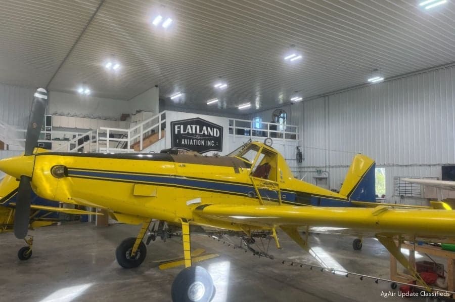 Yellow and blue agricultural aircraft parked inside a hangar with the Flatland Aviation logo.