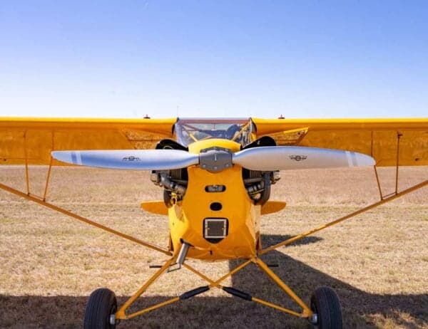 A head-on view of the yellow Legend Cub aircraft, registration N64HC, showing its propeller and exposed engine.