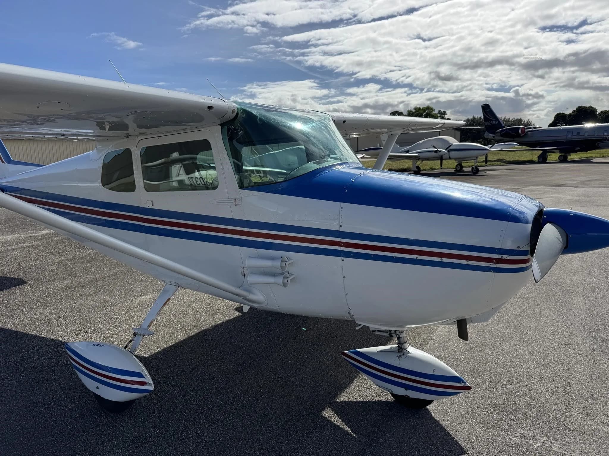 Close-up front-side view of a white and blue Cessna 172, showing the engine cowling and exhaust pipes.