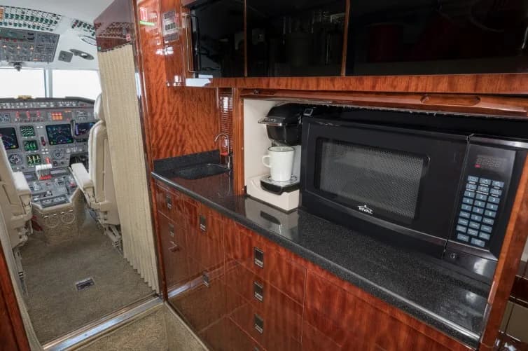 A luxurious aircraft galley with dark wood cabinetry, a microwave, and a coffee maker.