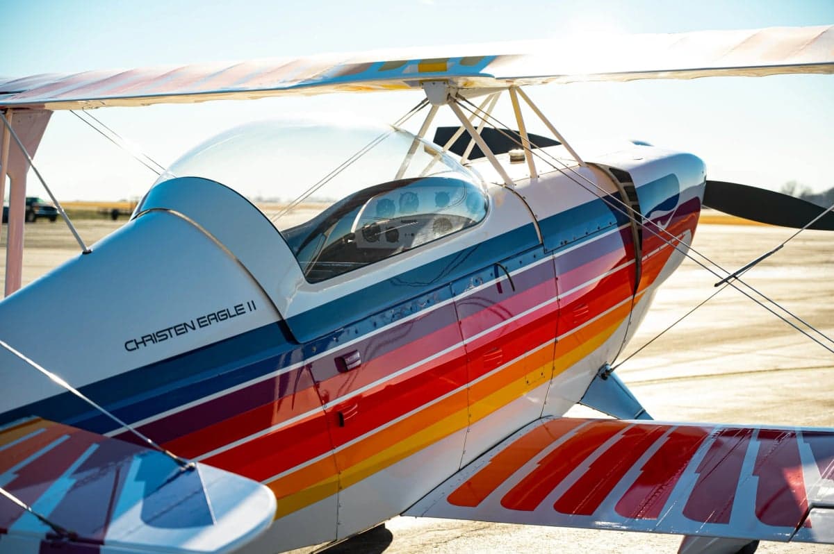 Close-up of the Christen Eagle II biplane showing the colorful paint scheme and cockpit door.