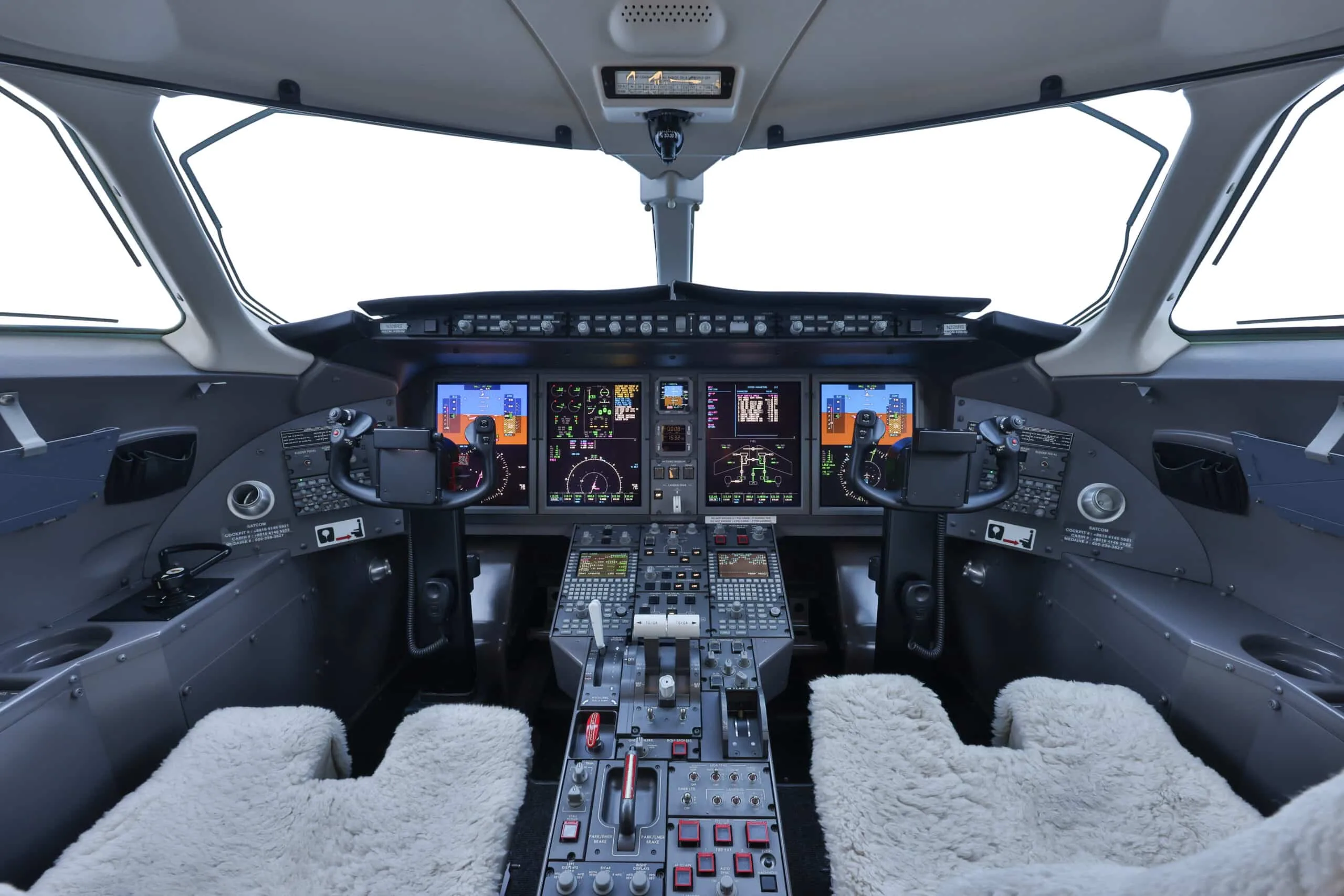 The modern cockpit of a private jet displays multiple digital screens and features sheepskin seat covers.
