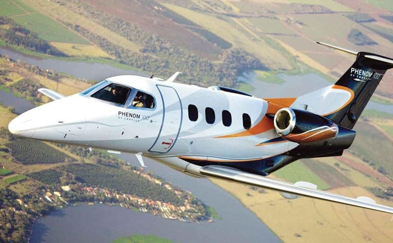 A Phenom 300 aircraft is in flight over a rural landscape.
