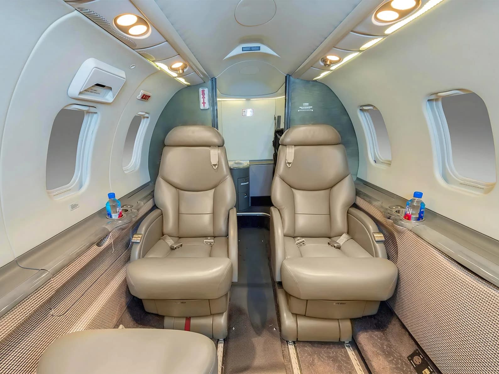 The aft cabin of a business jet with two beige leather seats facing forward and a galley area in the background.