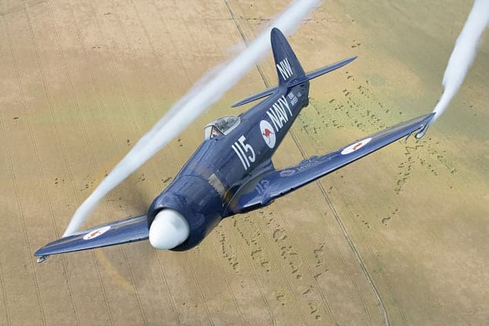 A close-up view of a blue aircraft in flight, showing the propeller and pilot.