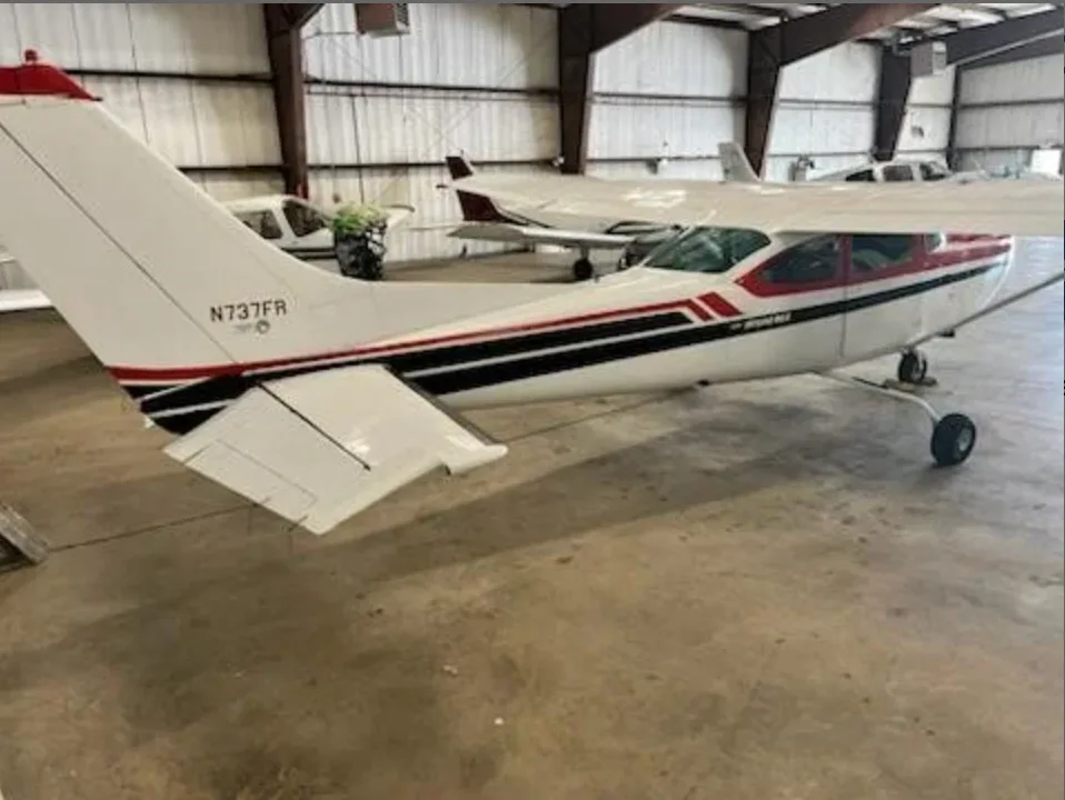 Rear-left view of a red and white Cessna 182 Skylane (N737FR) parked inside a hangar.
