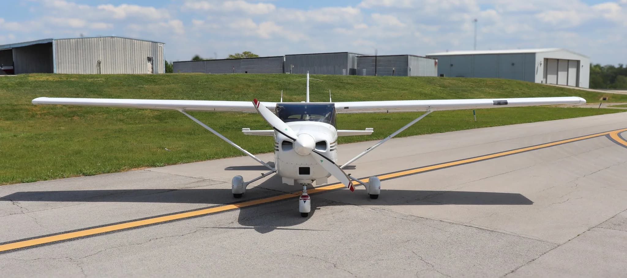 A head-on view of a white Cessna 182 Skylane with multi-color stripes on an airport runway.