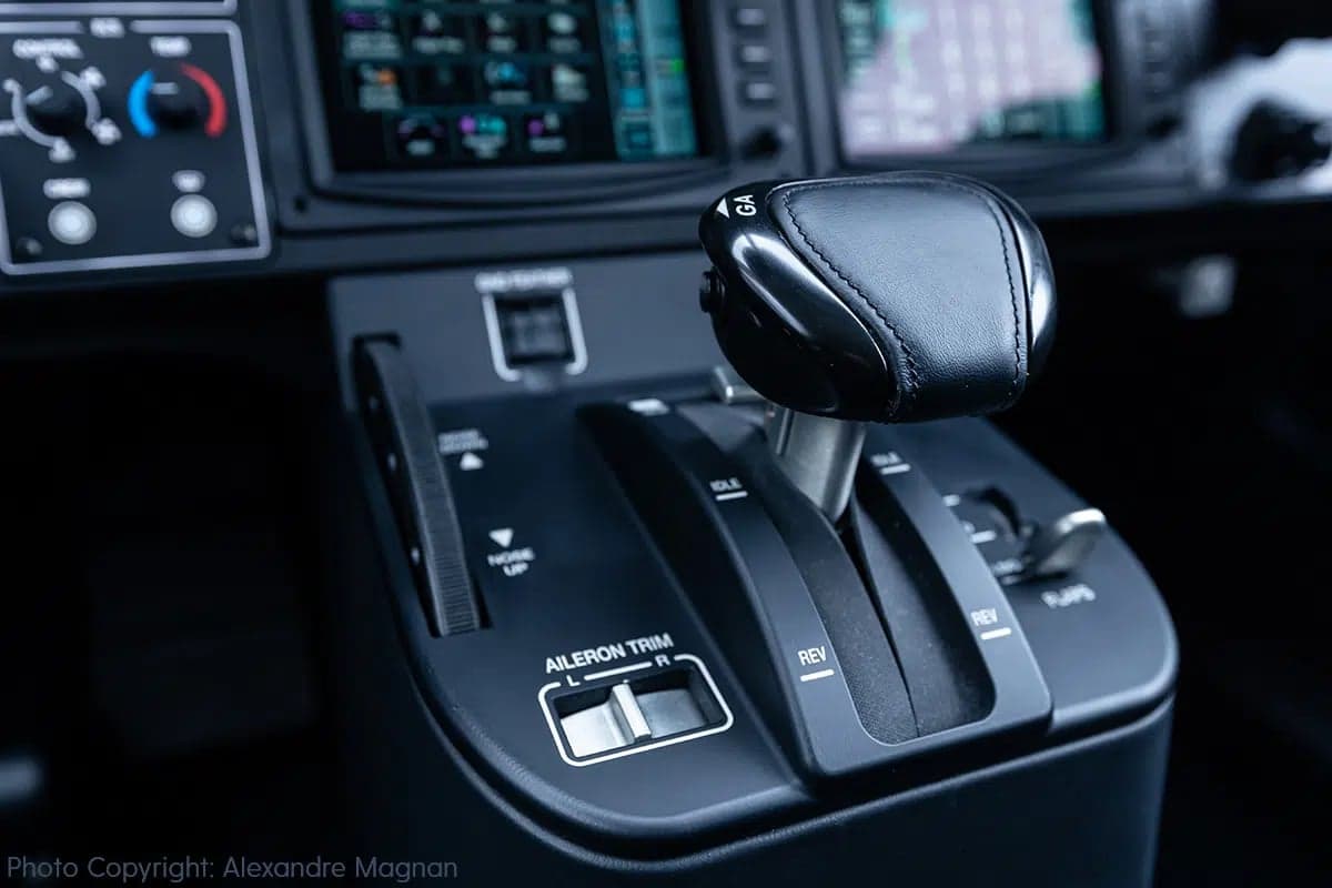A close-up view of the black throttle quadrant and aileron trim control in an aircraft cockpit.