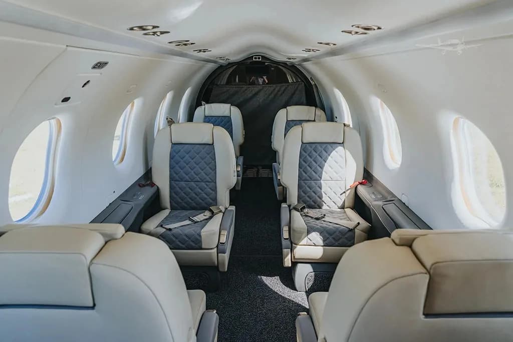 The aircraft cabin interior features multiple rows of light-colored seats with quilted blue inserts.