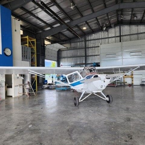Front view of a white and blue aircraft parked inside a hangar.