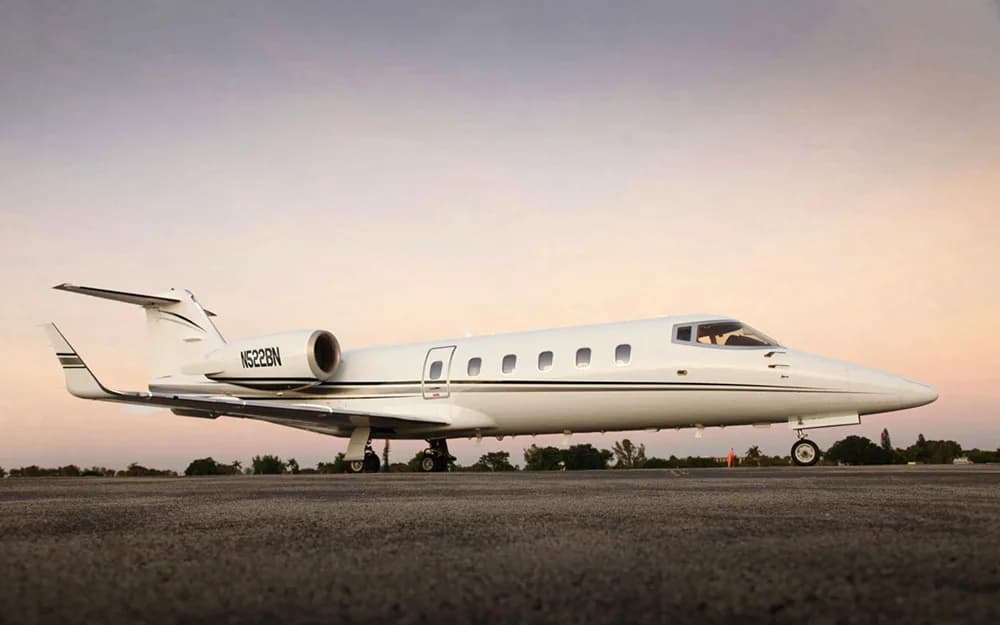 A white Learjet with black and grey stripes, tail number N522BN, parked on a tarmac at sunset.