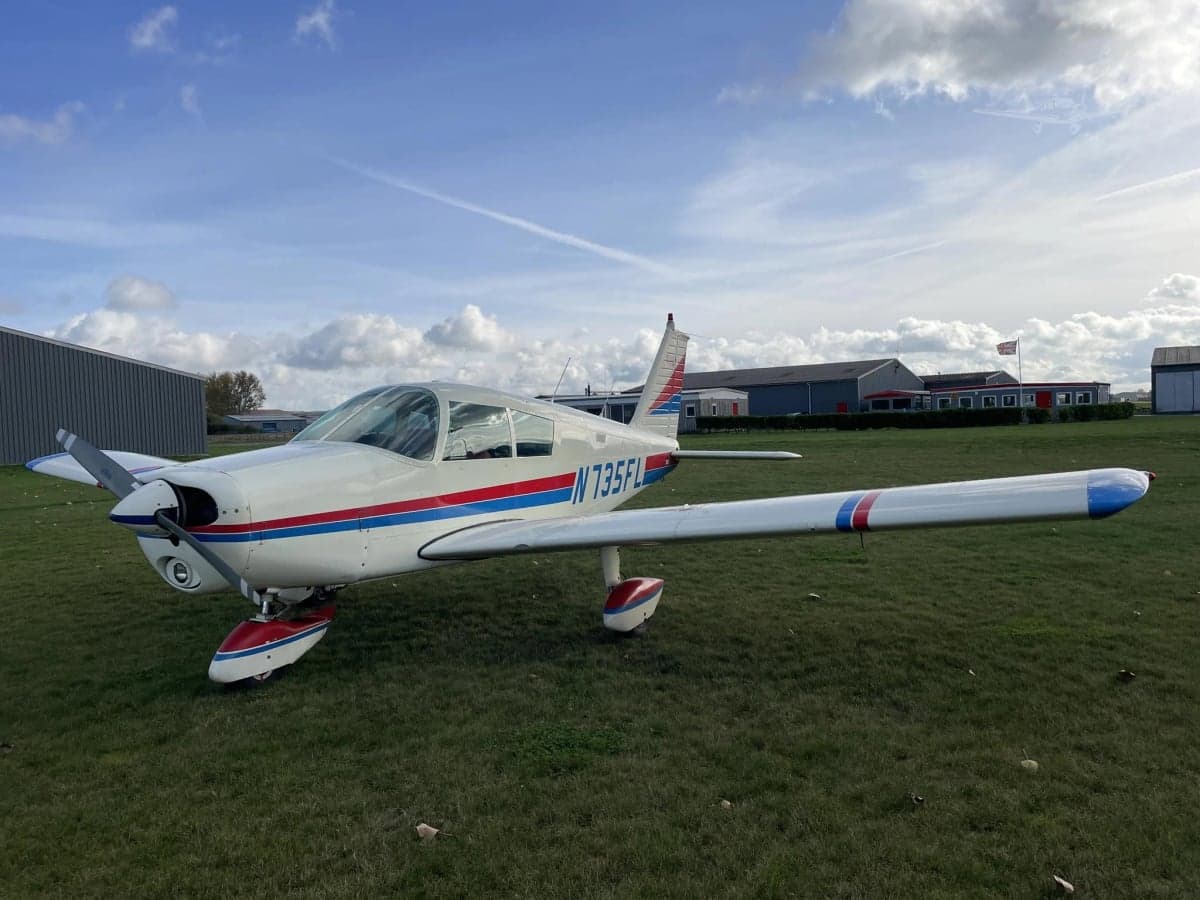 A Piper PA-28-181 Archer II aircraft, registration N735FL, is parked on a grassy field.