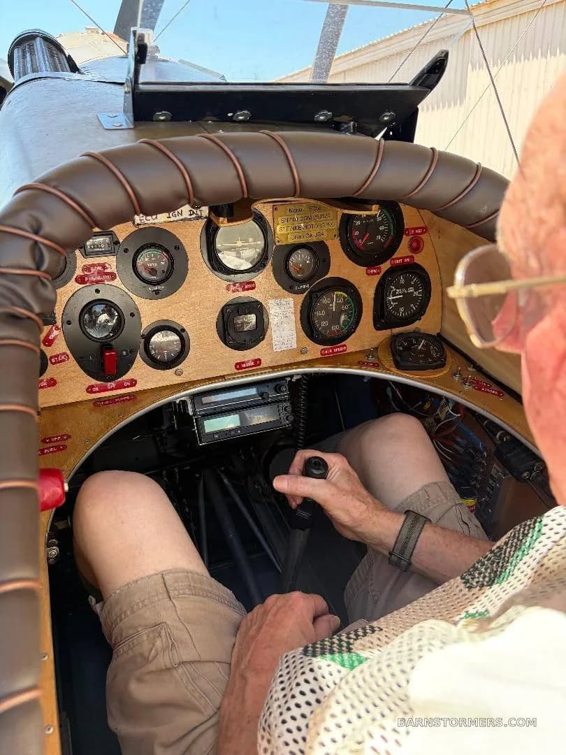 An overhead view of a pilot's legs and hands on the controls within a vintage-style aircraft cockpit.