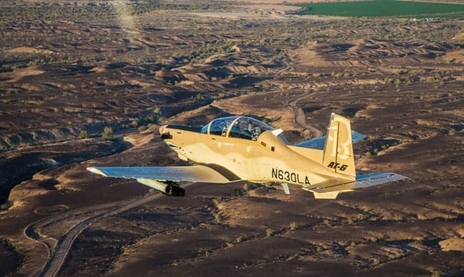 An AT-6 light attack aircraft flying over a desert landscape.