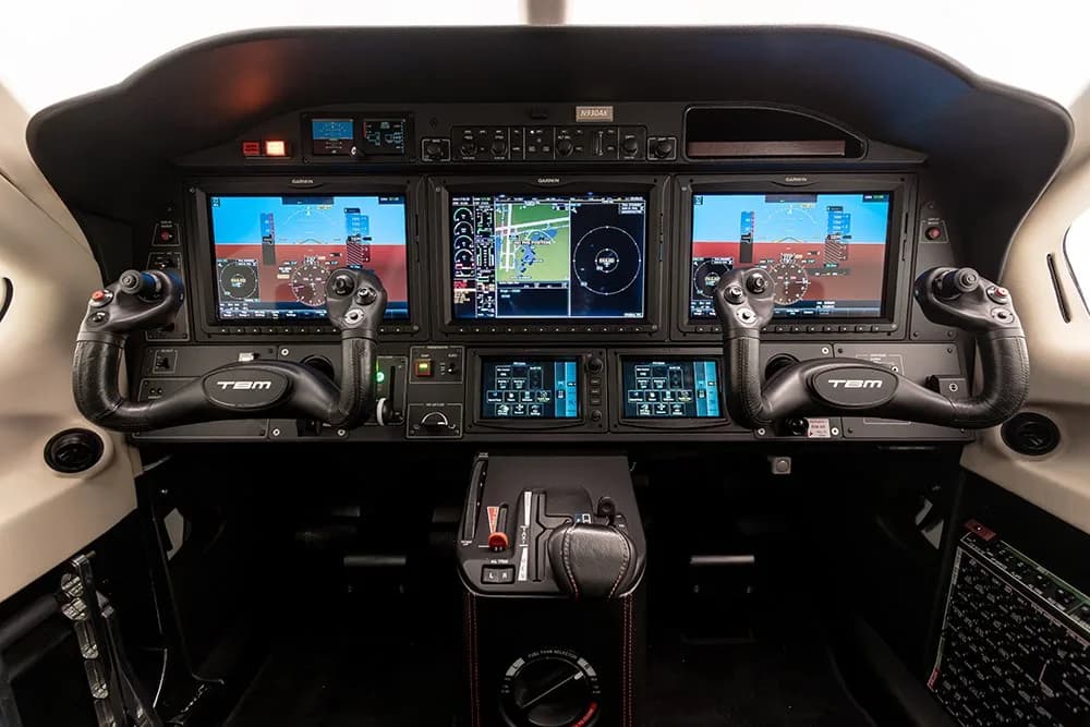The modern glass cockpit of a TBM 930 aircraft, featuring multiple display screens and control yokes.