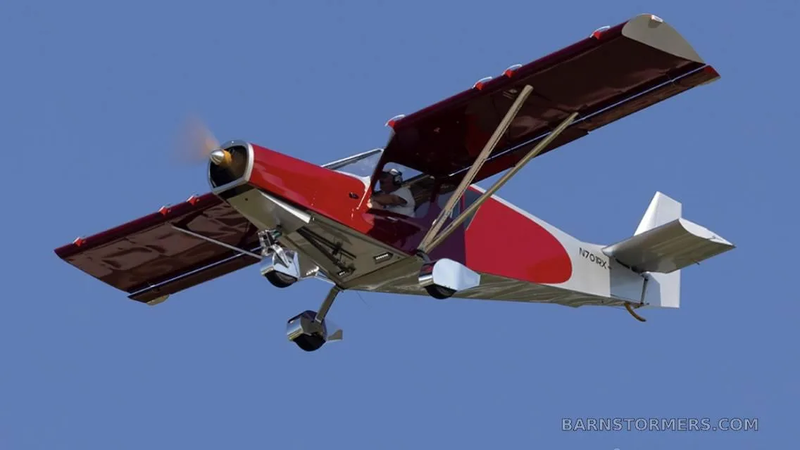 A red and silver single-engine aircraft with registration N70RX flying against a clear blue sky.