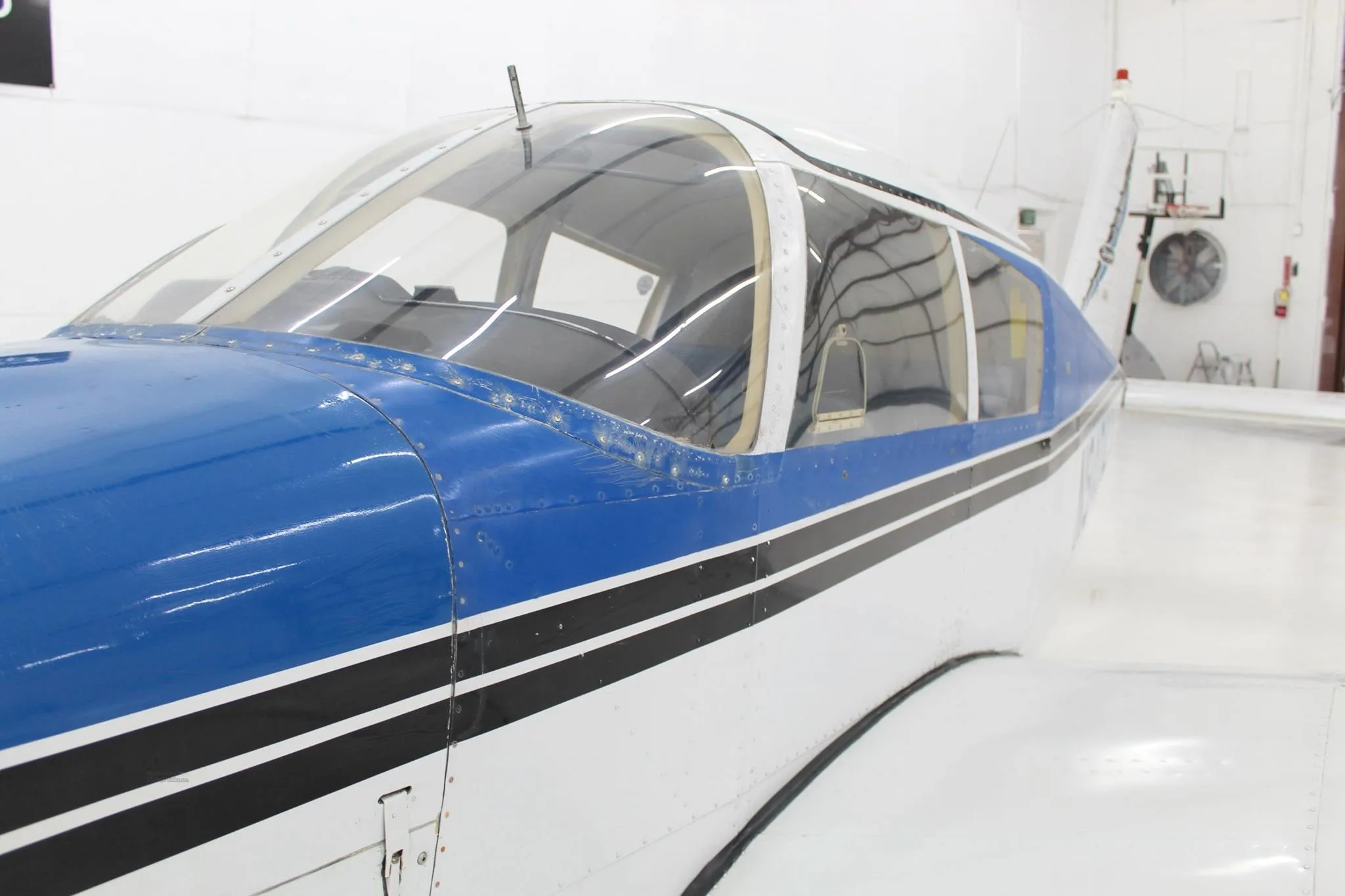 Close-up side view of the blue and white fuselage and cockpit canopy of a single-engine aircraft.
