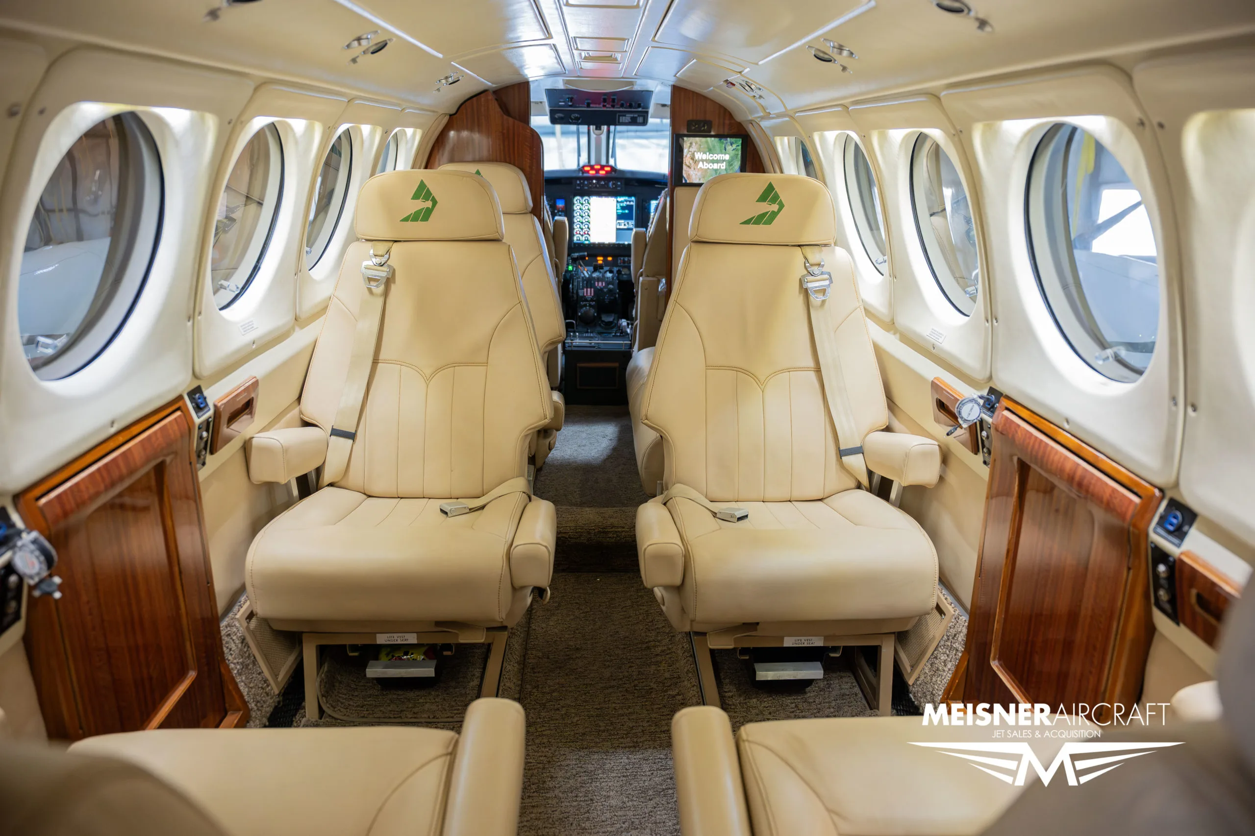 The interior cabin of an aircraft with beige leather seats and wood accents, looking towards the cockpit.