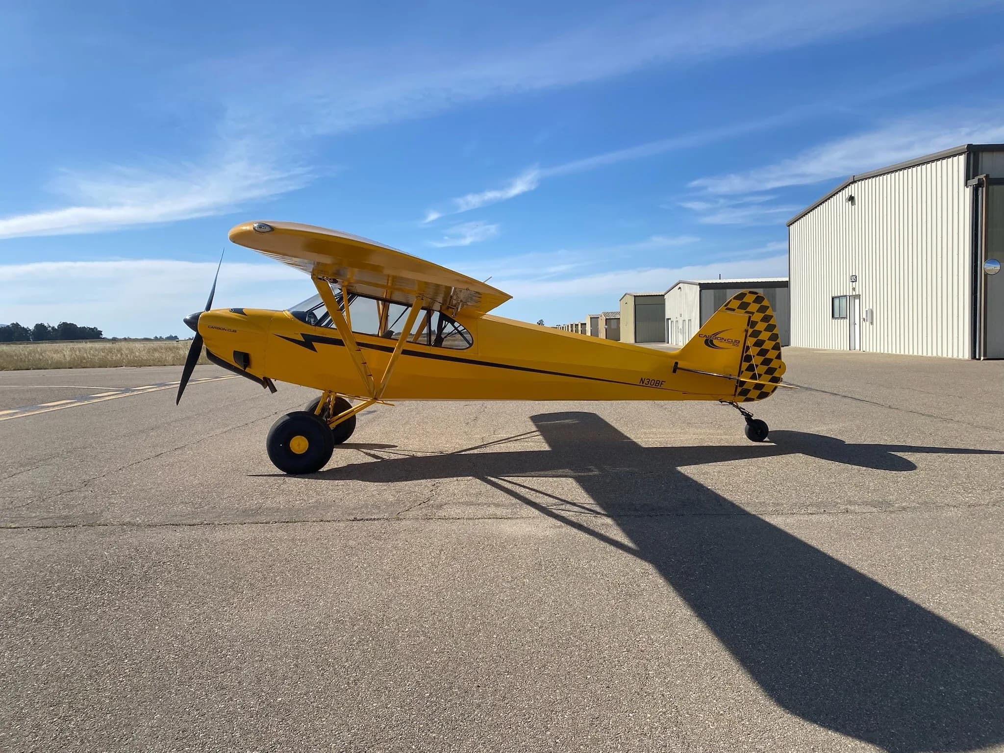 A yellow Carbon Cub aircraft with registration N30BF is parked on the tarmac next to a building.
