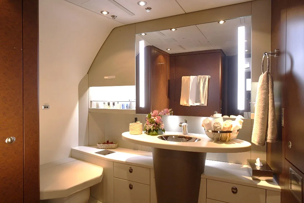 A well-appointed private jet lavatory featuring a vanity with a sink, mirror, and fresh flowers.