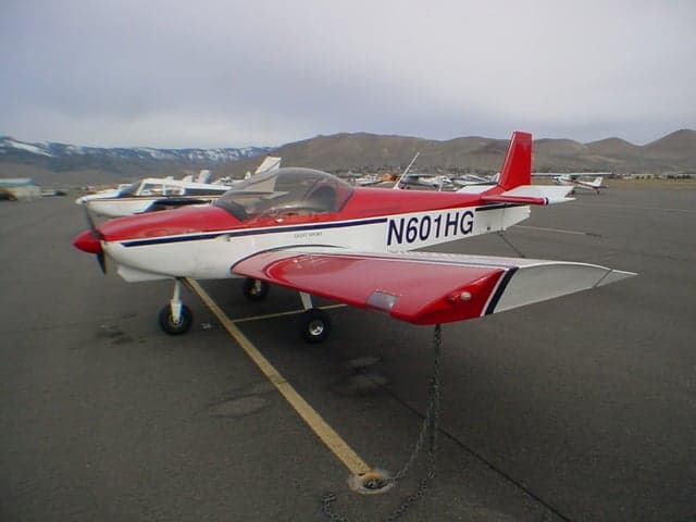A red and white light sport aircraft N601HG is parked on an airfield with snowy mountains in the background.