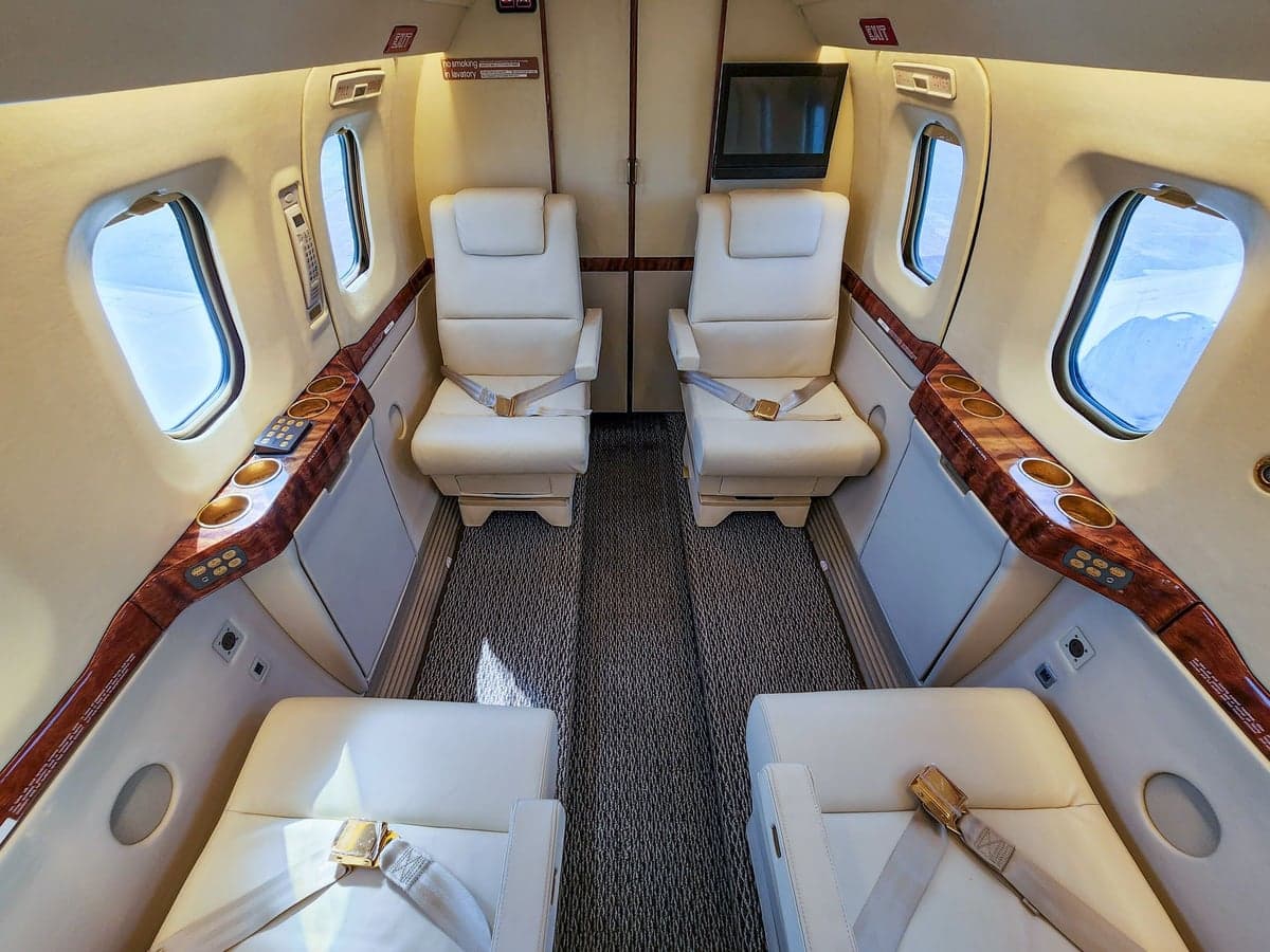 Aircraft cabin with white leather seats and wood trim.
