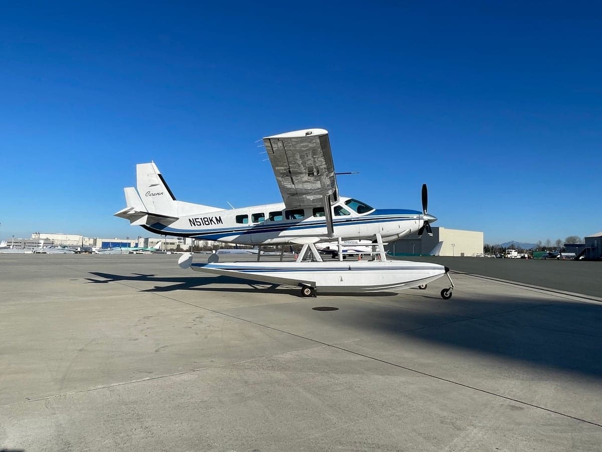 A side view of a white and blue Cessna Caravan on floats, parked on an airfield.