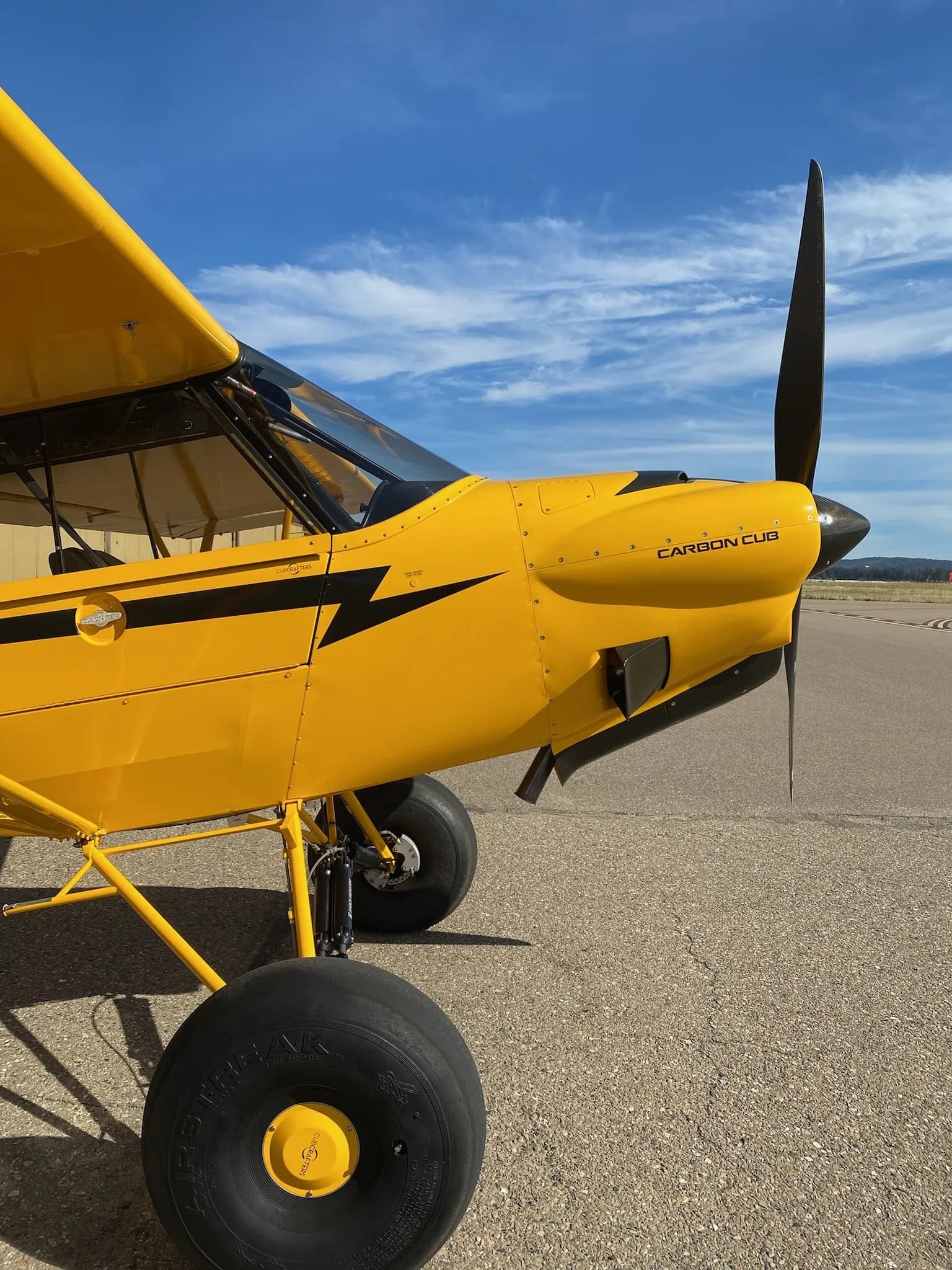 A yellow Carbon Cub aircraft is parked on the tarmac with a blue sky in the background.
