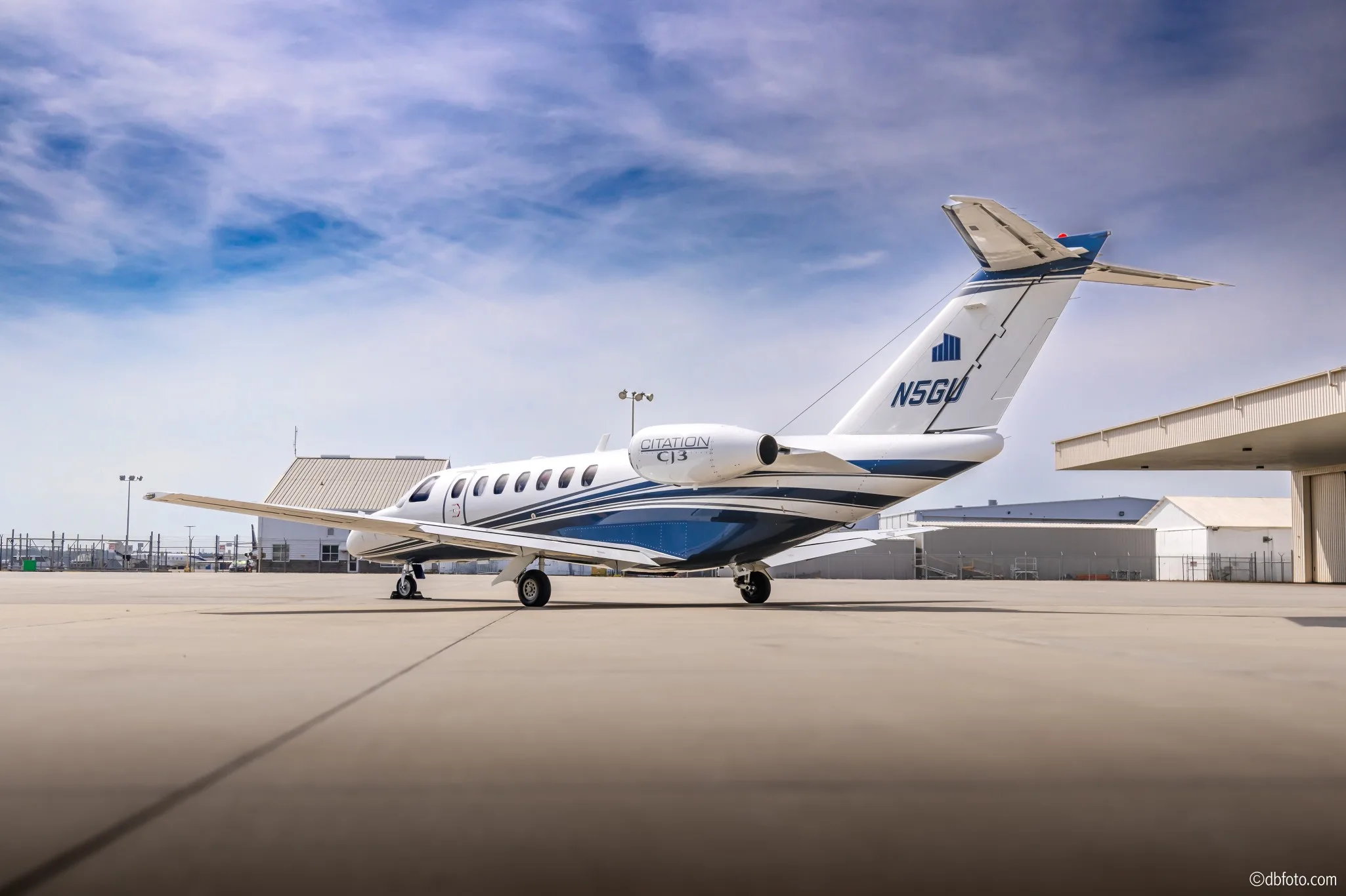 A rear-side view of a white Cessna Citation CJ3 business jet with blue and grey stripes, registration N5GU, parked on an airport tarmac.