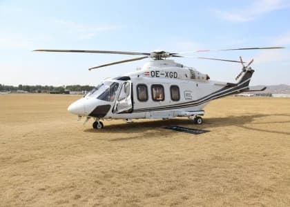 A white and black AgustaWestland AW169 helicopter is parked on a grassy field.