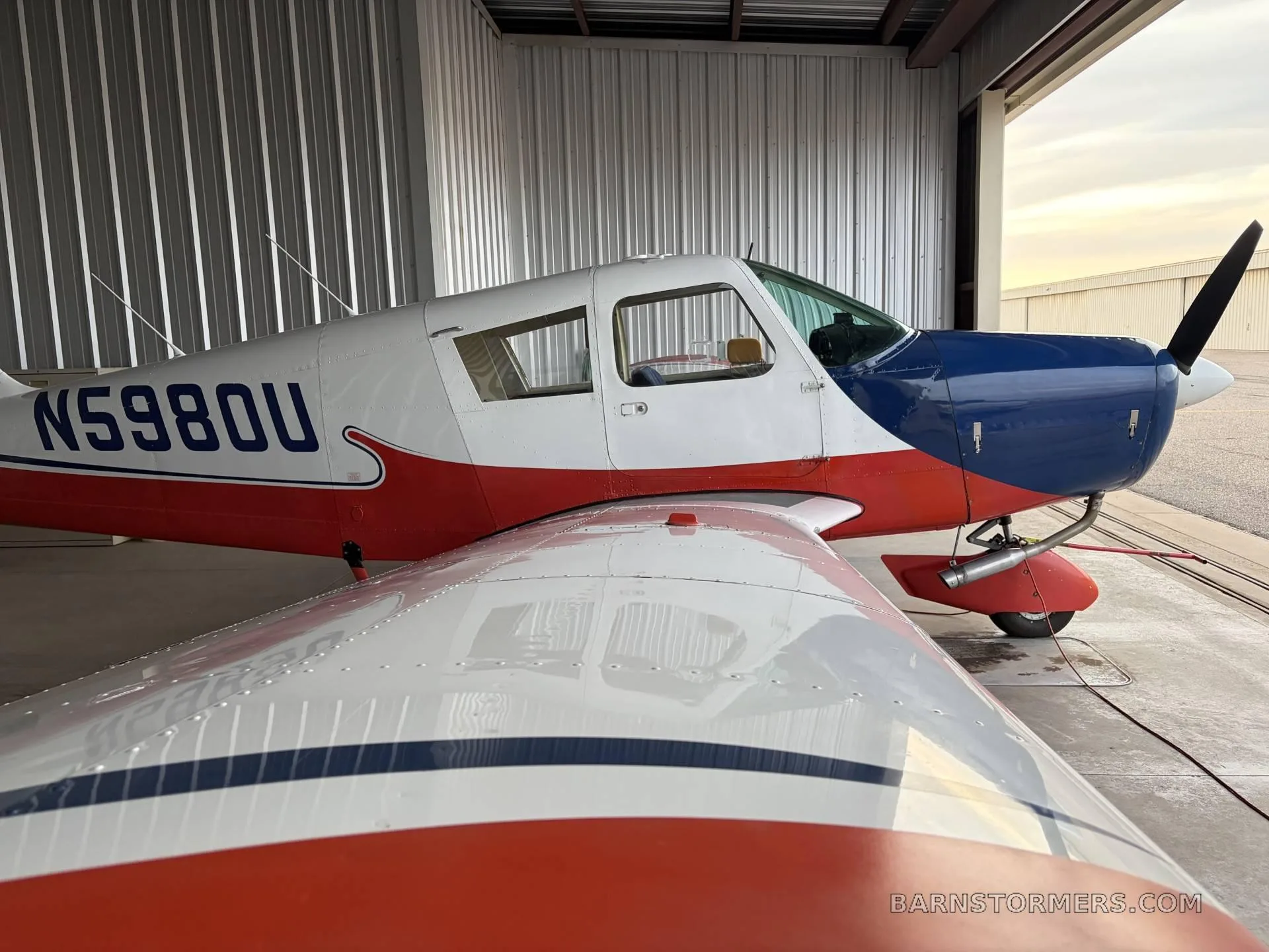 A close-up side view of the red, white, and blue single-engine propeller aircraft (N5980U) in a hangar.