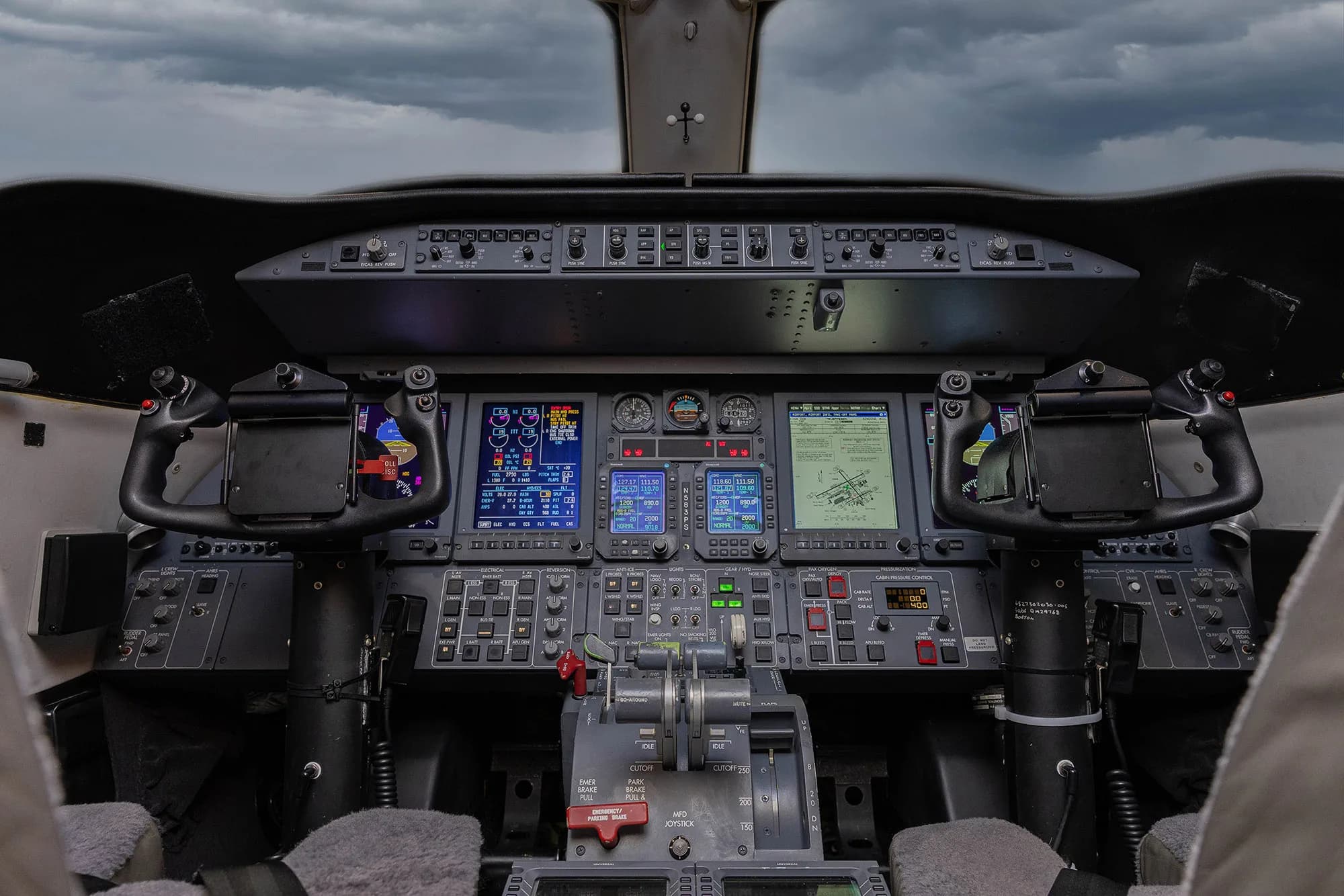 The cockpit of a business jet, featuring multiple digital displays, yokes, and a central control pedestal.