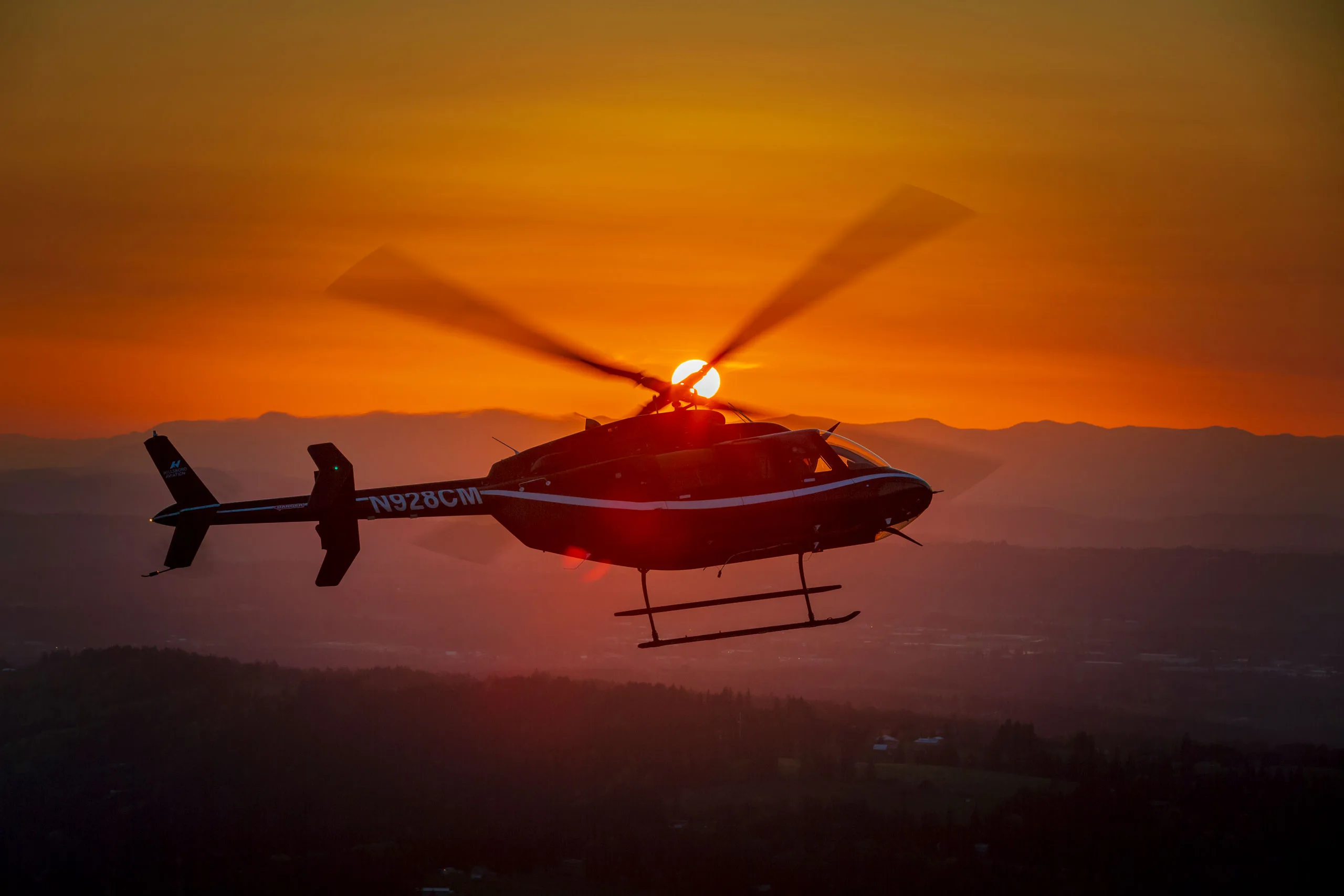 Helicopter flying silhouetted against a sunset.