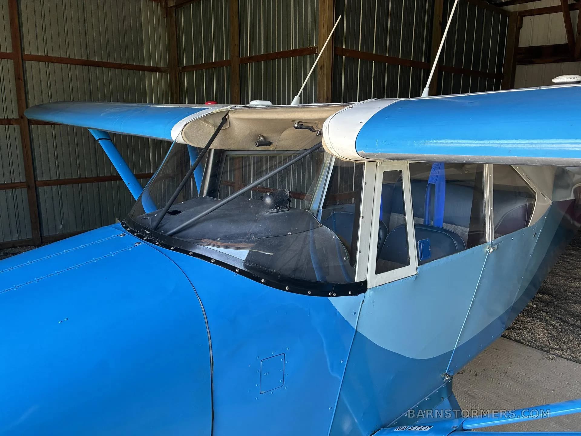A close-up view of the front fuselage and wing of a blue aircraft, parked inside a hangar.