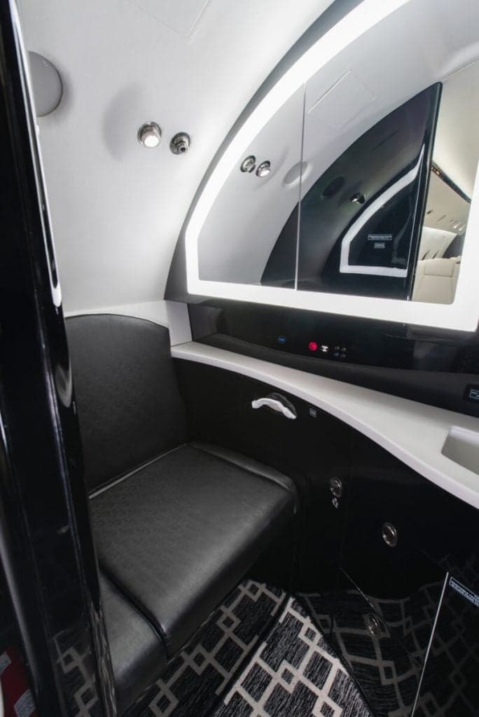 Close-up of the aircraft's lavatory with a black seat and illuminated mirror.
