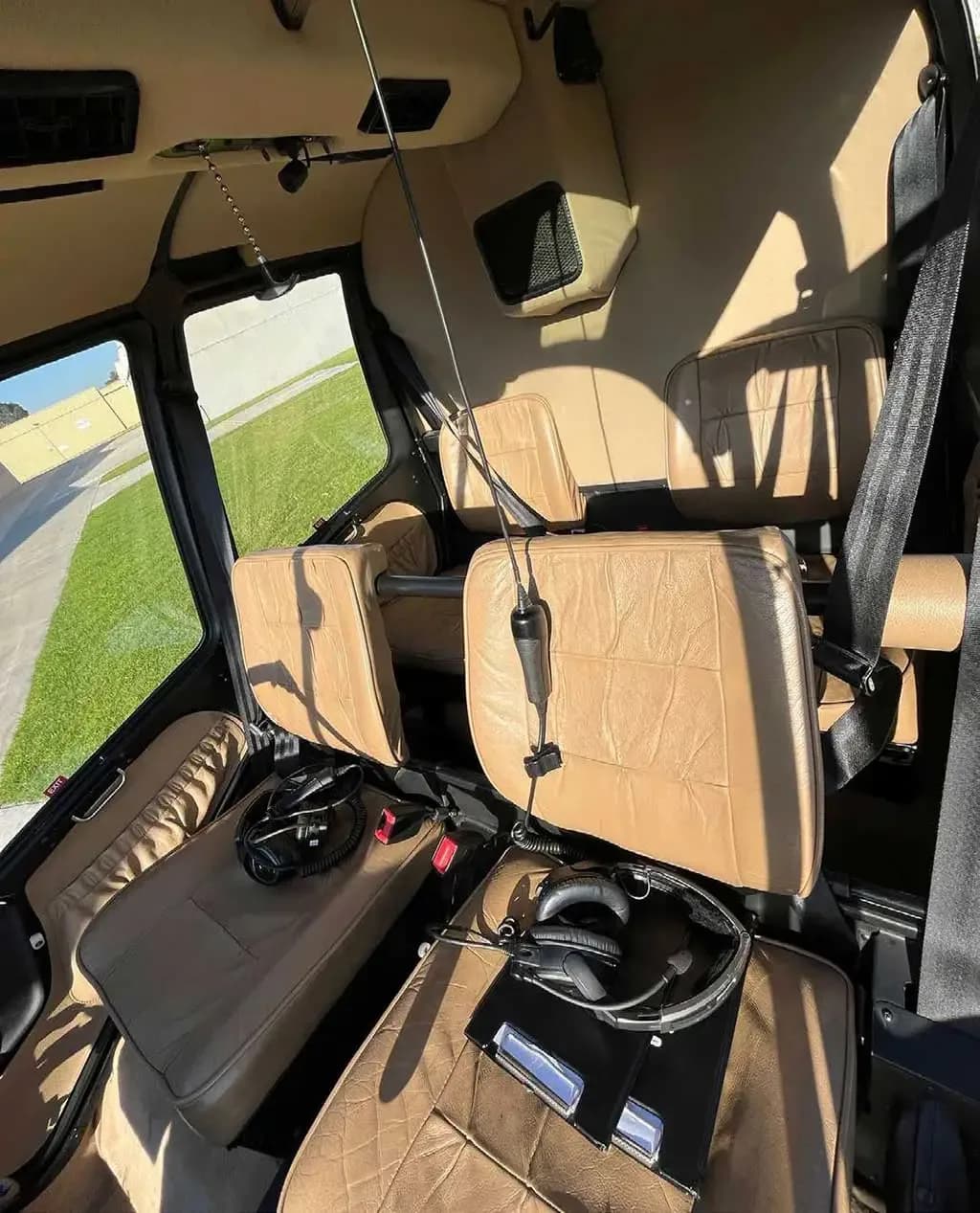 The tan leather interior cabin seats of a helicopter, with headsets on the front seats.
