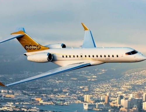 A white and gold Global jet flying over a city and harbor.