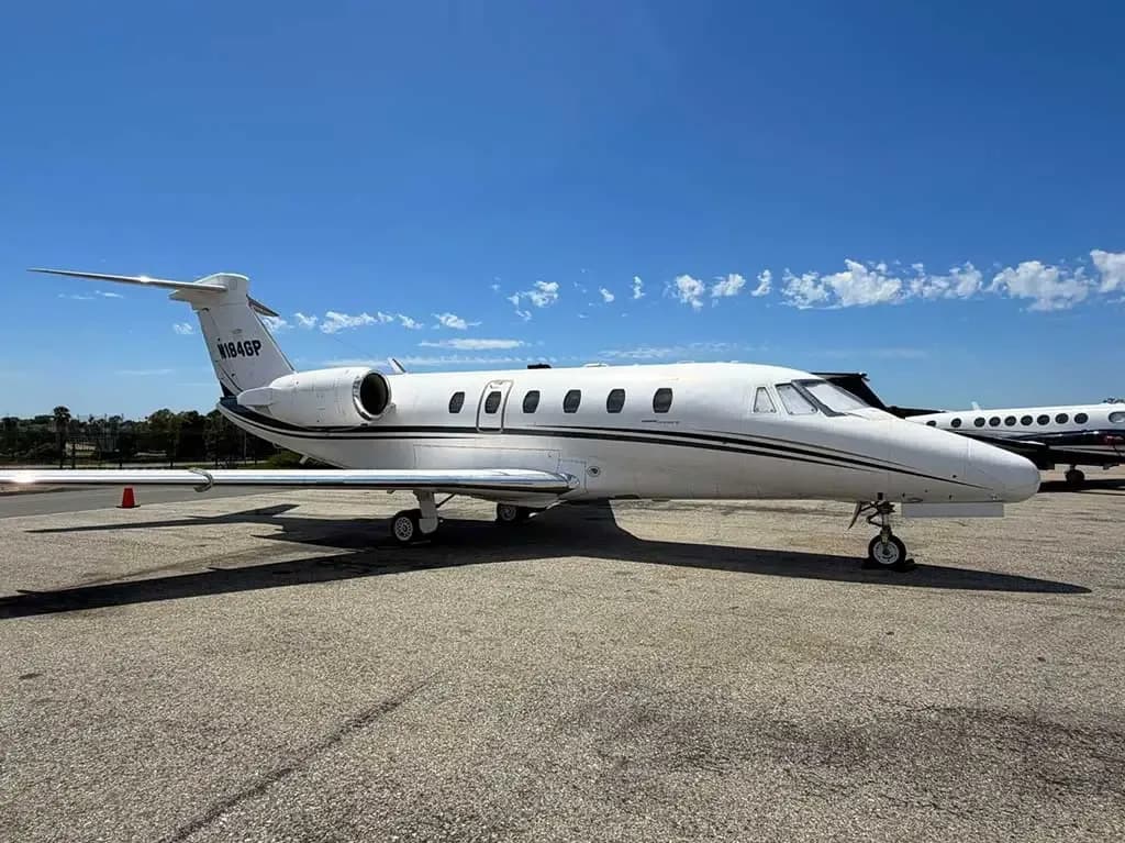 A white Cessna Citation business jet (N184GP) with a dark stripe, parked on an asphalt tarmac under a clear blue sky.
