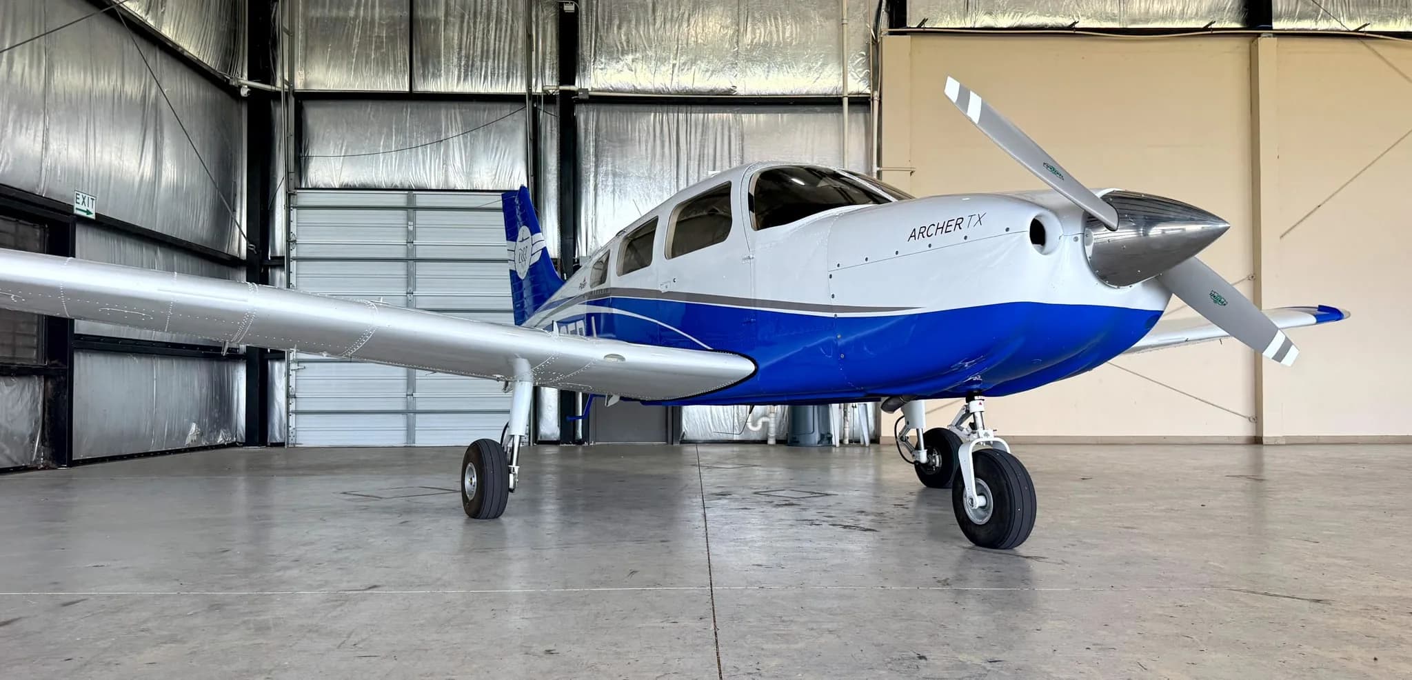 A front view of the white and blue Piper Archer TX aircraft, N105DJ, parked in a hangar.