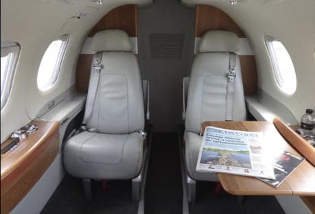 A view of the interior cabin of an aircraft with beige leather seats and wood trim.