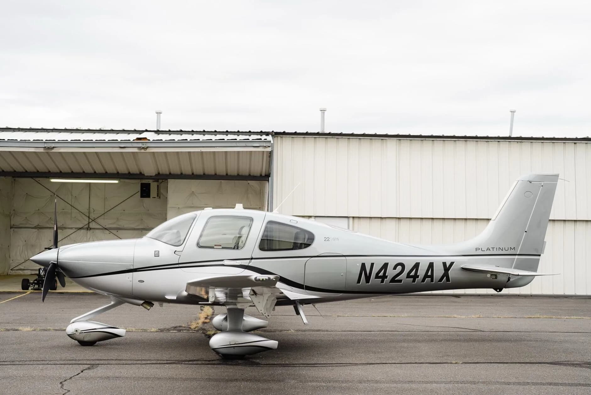 A silver Cirrus SR22 GTS Platinum aircraft, N424AX, is parked on an asphalt tarmac with hangars in the background.