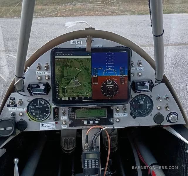 The cockpit of an experimental ultralight aircraft shows a tablet displaying navigation and flight instruments, along with analog gauges and a radio.