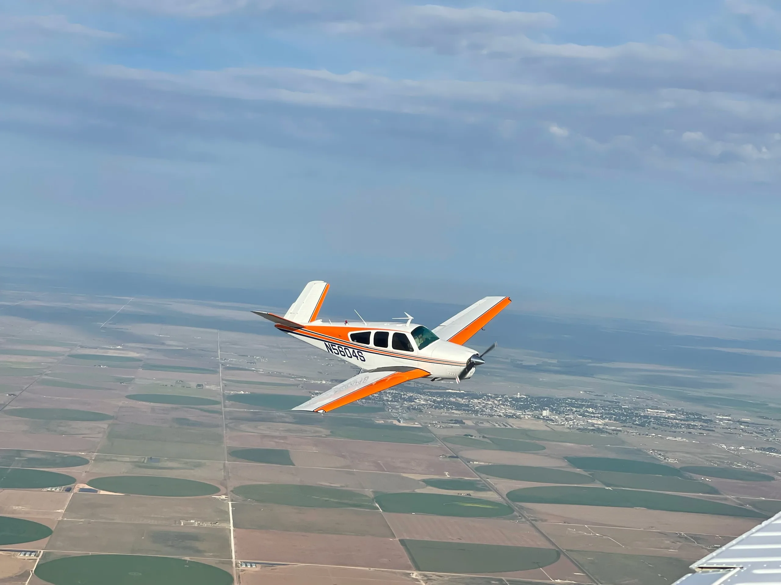 A Beechcraft V35 Bonanza aircraft in flight with an orange and white paint scheme.