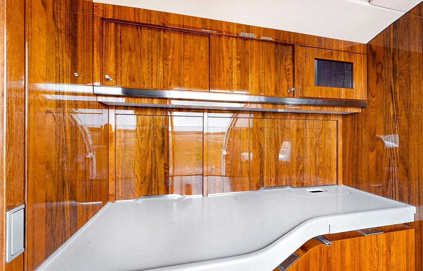 A close-up view of the private jet's galley area with polished wooden cabinetry and a white countertop.