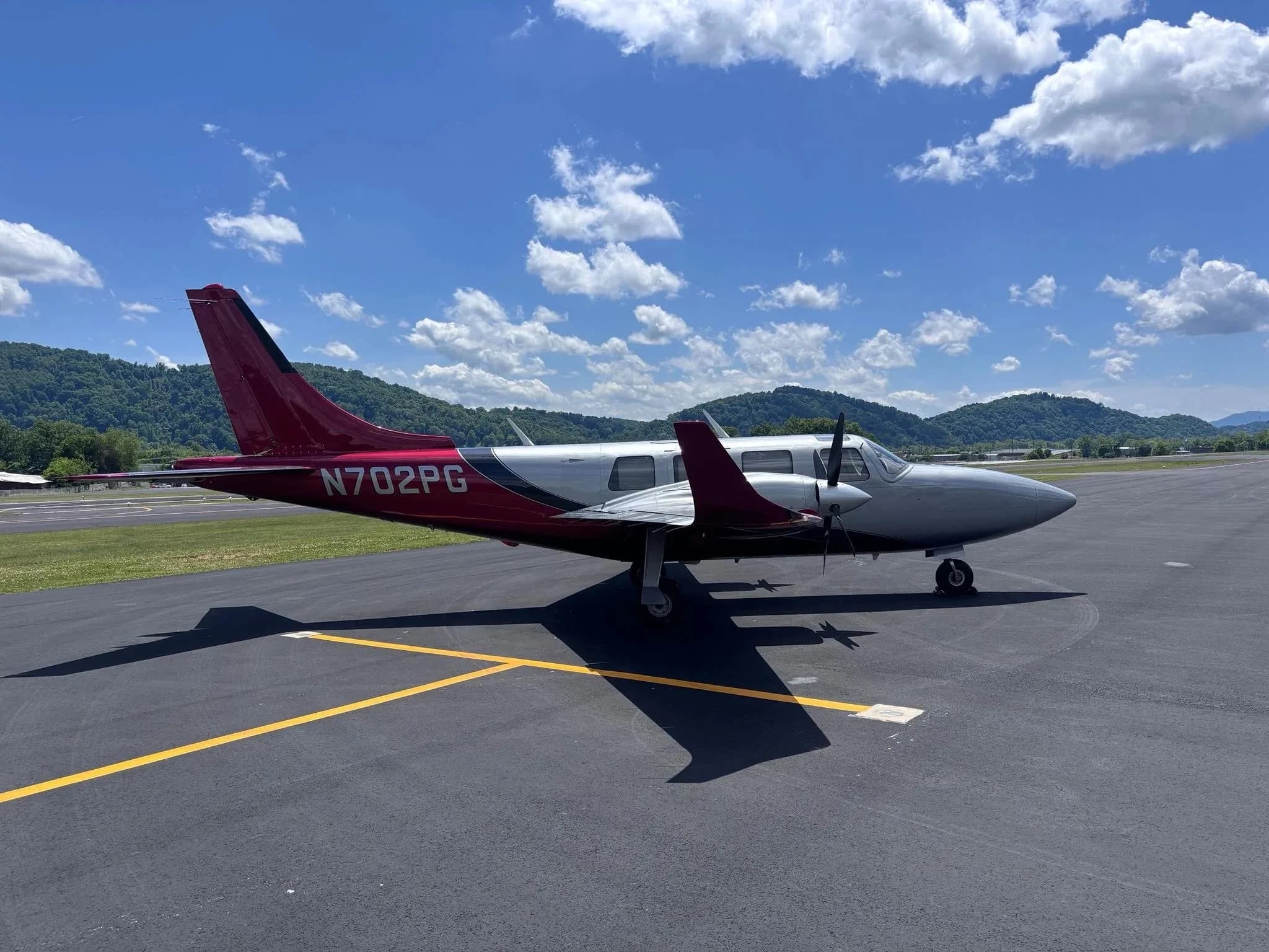A three-quarter front view of a silver and red twin-engine Aerostar aircraft (N702PG) on an airfield.
