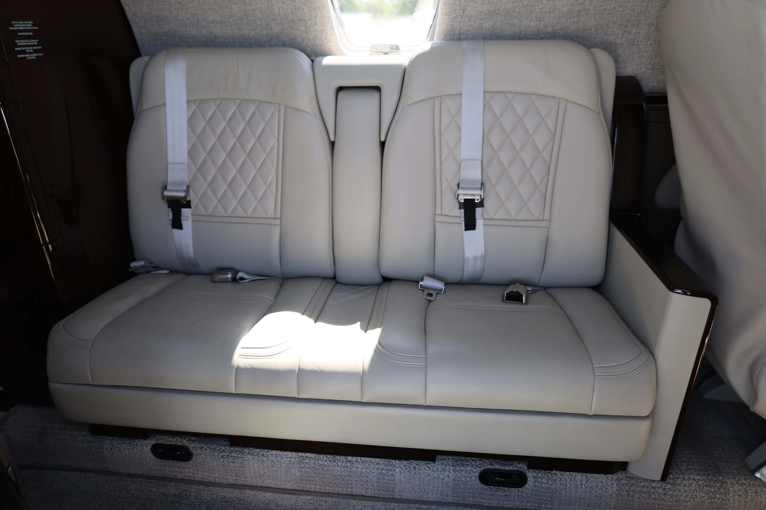 A close-up of two light-colored leather seats with quilted patterns and seatbelts in a private jet cabin.
