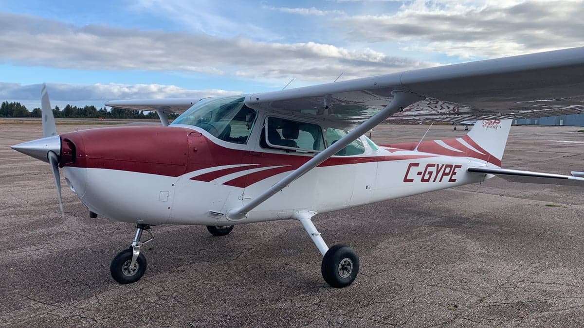 A white and red Cessna 172 (C-GYPE) parked on an asphalt tarmac under a cloudy sky.