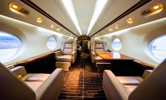 Interior of a private jet with leather seats and a wooden table.
