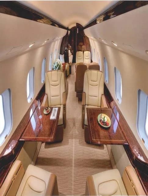 A luxurious aircraft cabin interior with beige leather seats, polished wood tables, and a floral centerpiece.