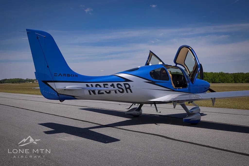 A rear-side view of the blue and silver Cirrus SR20 aircraft (N251SR) with open doors on an airfield.